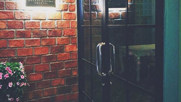 A brick wall with a sign reading "DNA Pannat Nikhon Hotel" and a glass door with a handle.