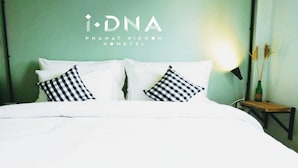 A hotel room with a bed, two checkered pillows, a nightstand with a lamp, and a wall with the hotel name.