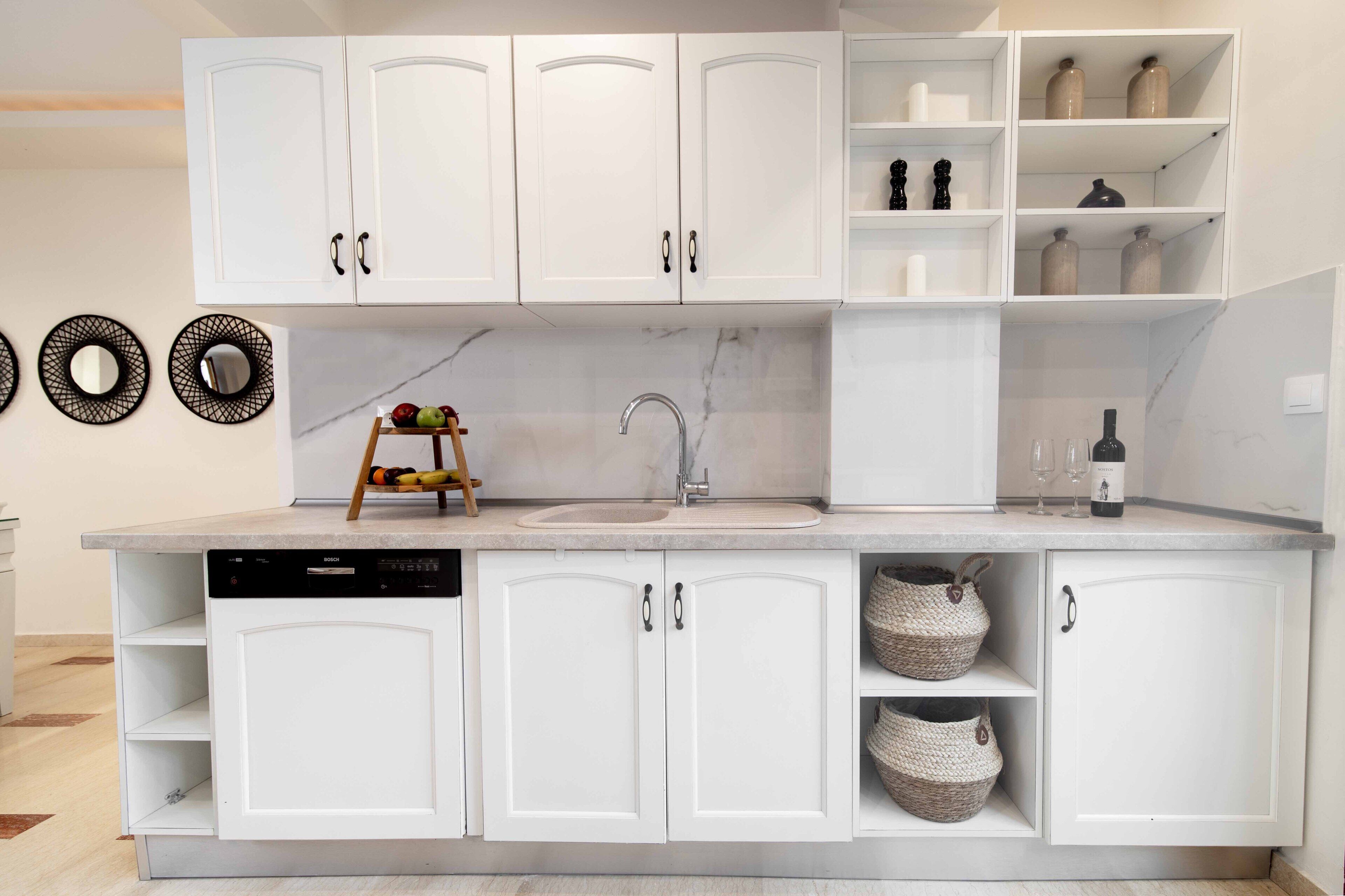 A modern kitchen with white cabinetry, a built-in dishwasher, and a marble backsplash.