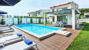 Une piscine dotée de chaises longues et d’une pergola, entourée d’une terrasse en bois et d’une pelouse.