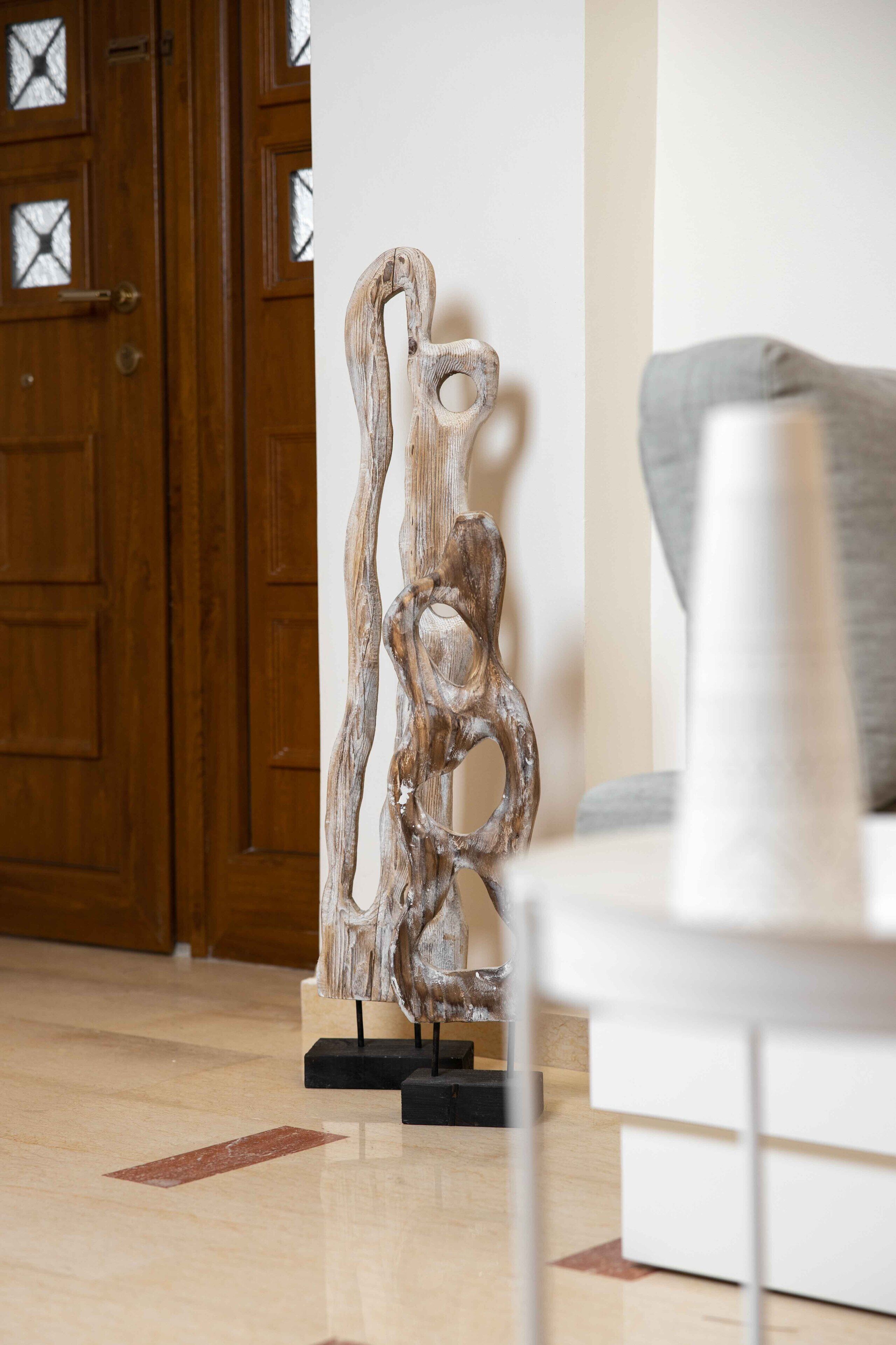 A wooden sculpture on a black stand in a room with a wooden door and a white couch.