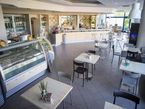 Un café moderno con barra central, diferentes disposiciones de asientos y una vitrina.