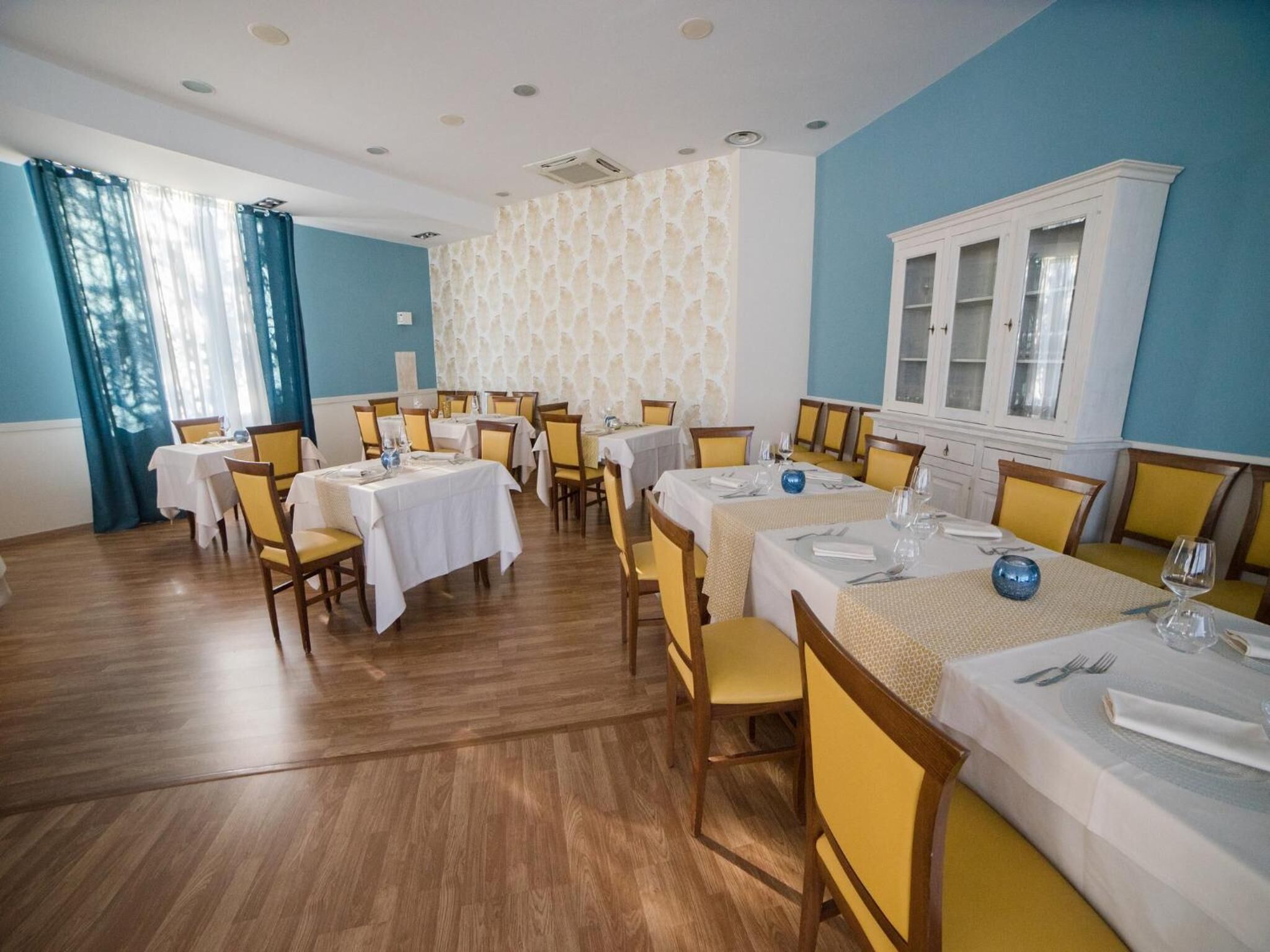 A dining area with multiple tables and chairs, a patterned wall, and a cabinet with glass doors.