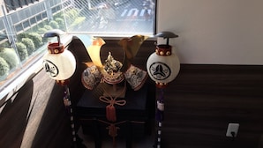A room with a view of a cityscape through a window, a small table with decorative items, and a power outlet on the wall. -  bnb+ Shinbashi - Hostel (Tokyo)