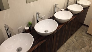 A bathroom with three white sinks, a wooden vanity, and a stone-tiled floor. -  bnb+ Shinbashi - Hostel (Tokyo)