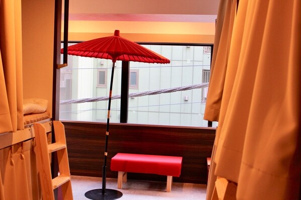 A room with a red bench, a floor lamp, and a view of buildings through a window.