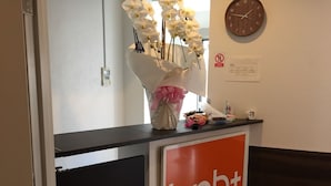 A reception desk with a 'bnb+' sign, a clock, and a bouquet of white flowers. -  bnb+ Shinbashi - Hostel (Tokyo)