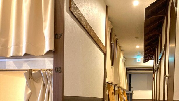 A hotel corridor with wooden flooring, a wooden staircase, and a view of a room with a bed and curtains. -  bnb+ Shinbashi - Hostel (Tokyo)