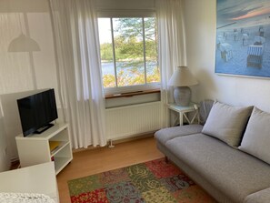 A living room with a television, a sofa, a lamp, a radiator, and a window with curtains.