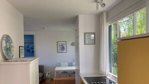 Kompakti keittiö, jossa on sisäänrakennettu liesi, ikkuna, josta avautuu näkymä vehreään maisemaan, sekä ruokailutila, jossa on penkki ja tuoleja.