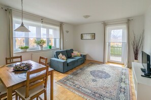 A living room with a sofa, a dining table with chairs, a large rug, and a TV on a stand. - Apartments Vila Marjetica (Bled)