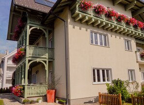 A multi-story building with balconies adorned with flowers, a large potted plant, and a wooden fence. - Apartments Vila Marjetica (Bled)