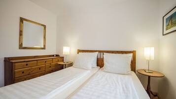 A double bed with white linens, a wooden dresser, two bedside tables with lamps, and a framed picture on the wall.