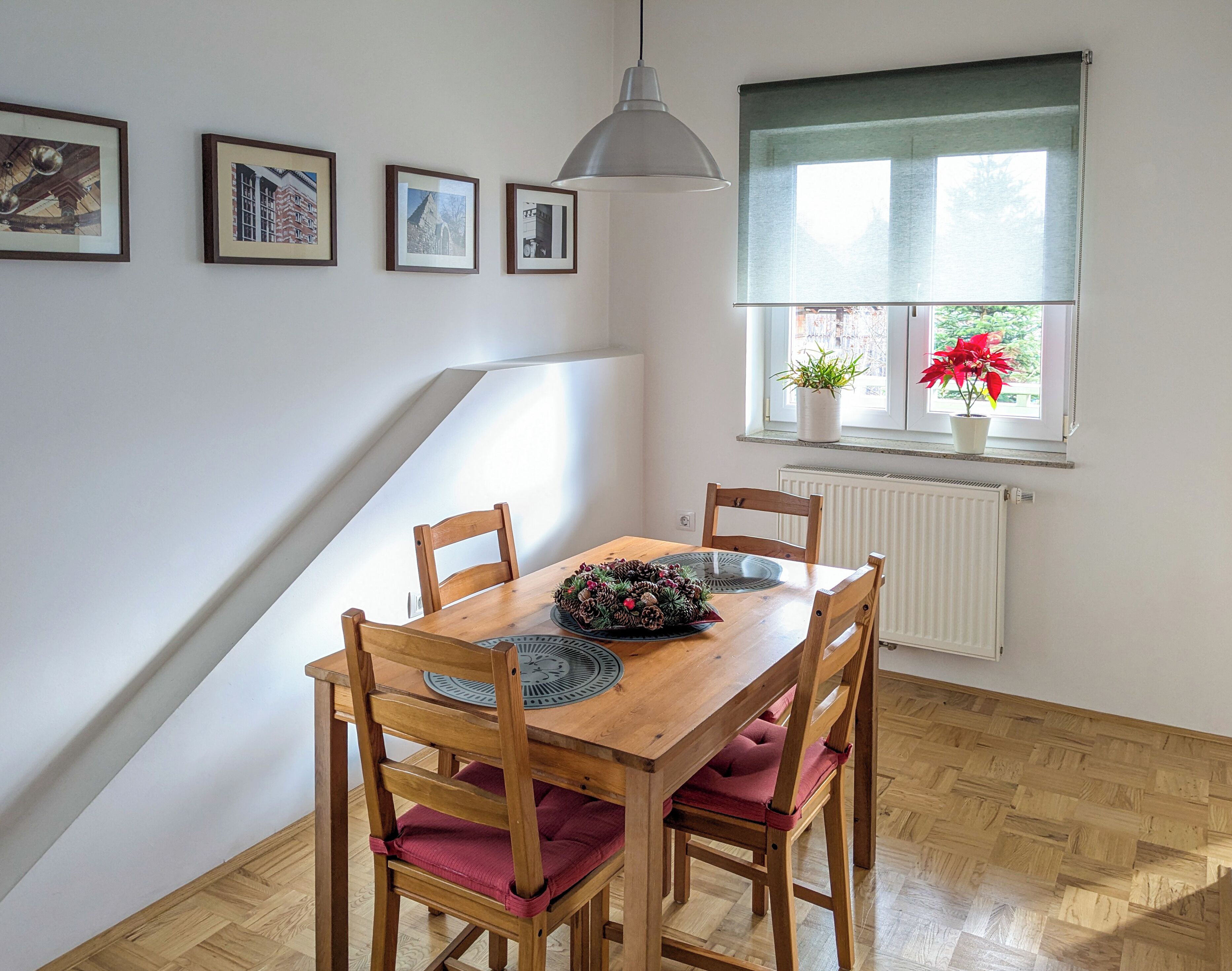 A dining area with a wooden table, four chairs, a pendant light, and framed pictures on the wall.