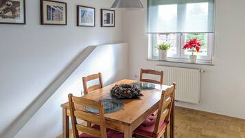 A dining area with a wooden table, four chairs, a pendant light, and framed pictures on the wall.