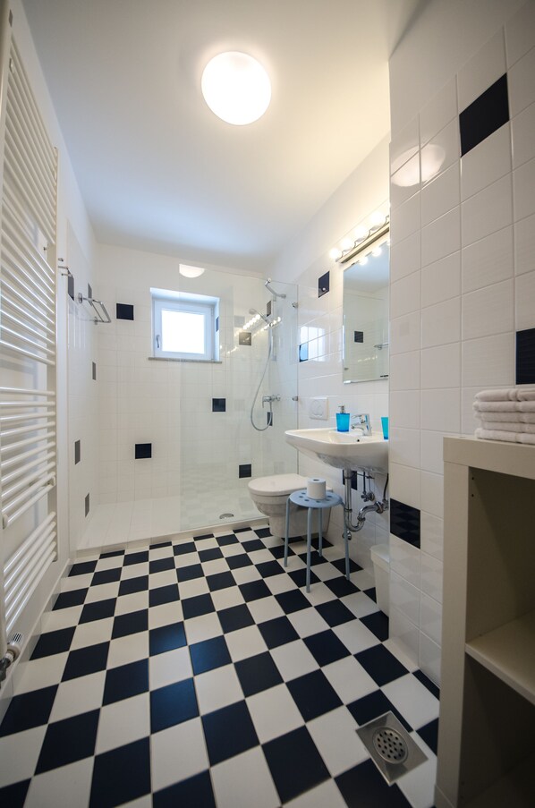 Un baño con piso a cuadros, lavamanos, inodoro, ducha y ventana.