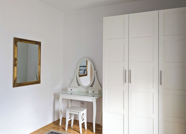 A white vanity with a mirror, a small stool, and a wardrobe with two doors. - Apartments Vila Marjetica (Bled)