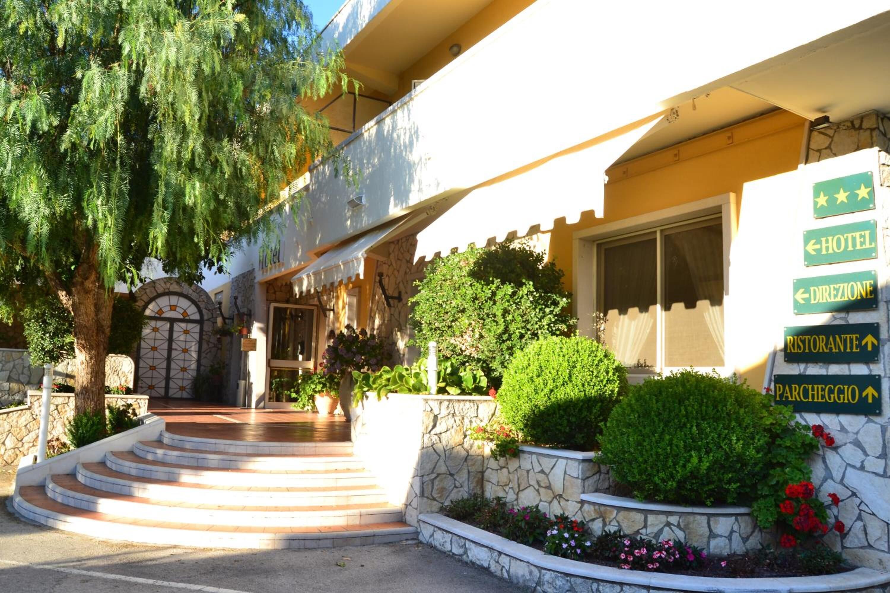L’entrée d’un hôtel, avec une façade en pierre, un escalier menant à l’entrée et des panneaux indicateurs pour l’hôtel, le restaurant et le parking.