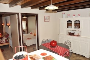 A cozy room with a bed, a dining table with a red tablecloth, and a white cabinet with glass doors.