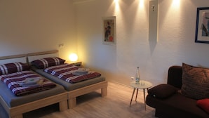 Une chambre avec deux lits simples, une petite table, un canapé et un luminaire fixé au mur.