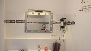 Un baño con lavamanos, espejo, secador de pelo y toallero.
