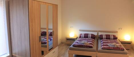 A bedroom with two beds, a wardrobe, bedside lamps, and a radiator.