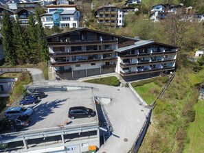 A multi-story building with balconies, a parking area, and a surrounding landscape.