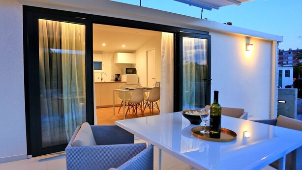 An outdoor dining area with a table and chairs, a bottle of wine, and a bowl of bread. - MENDULA RESORT (Nin)