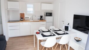 A modern kitchen with white cabinetry, a wooden countertop, a microwave, and a dining area with white chairs and a table set for four. - MENDULA RESORT (Nin)