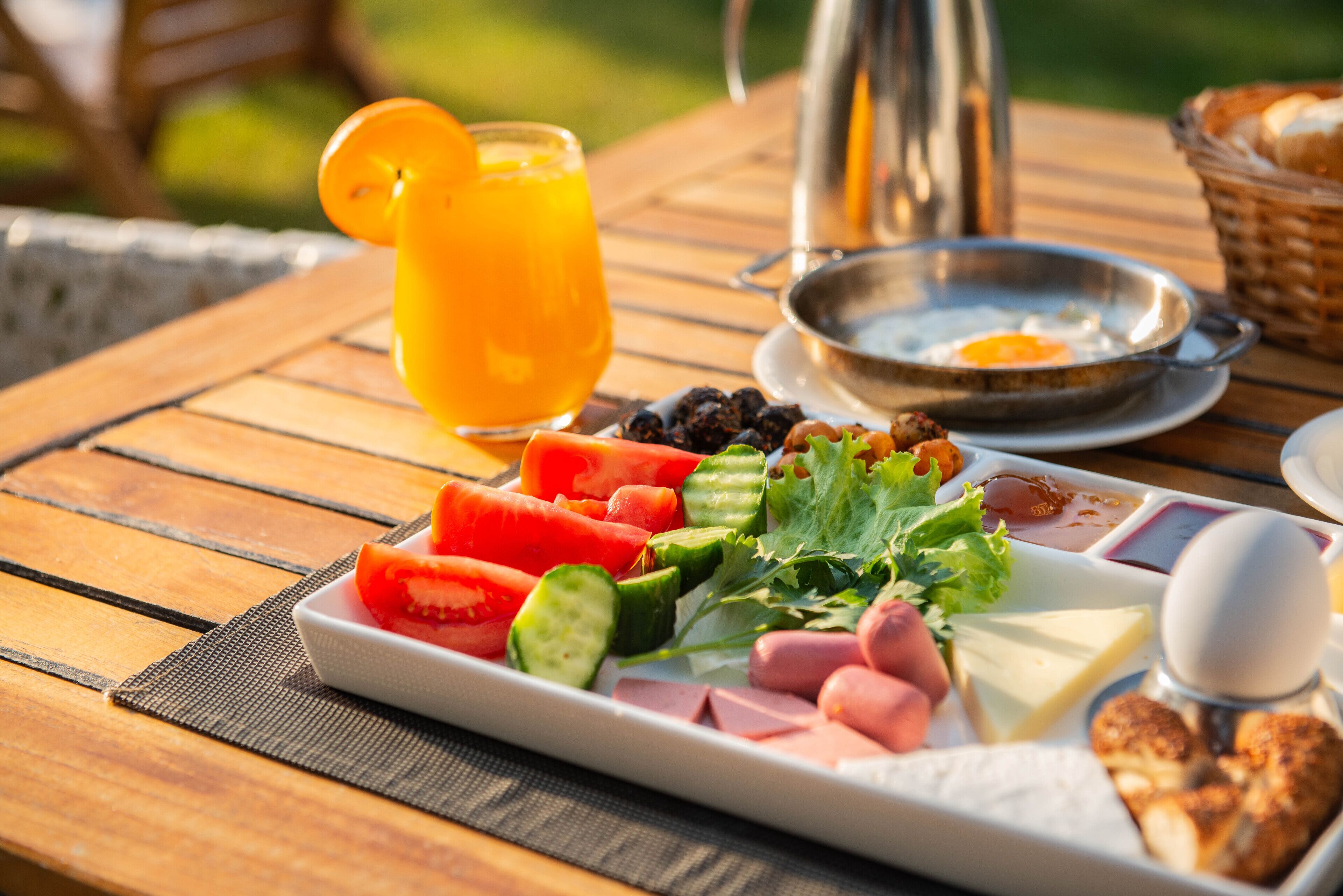 Un desayuno con un plato de comida, un vaso de zumo de naranja y un hervidor sobre una mesa de madera.