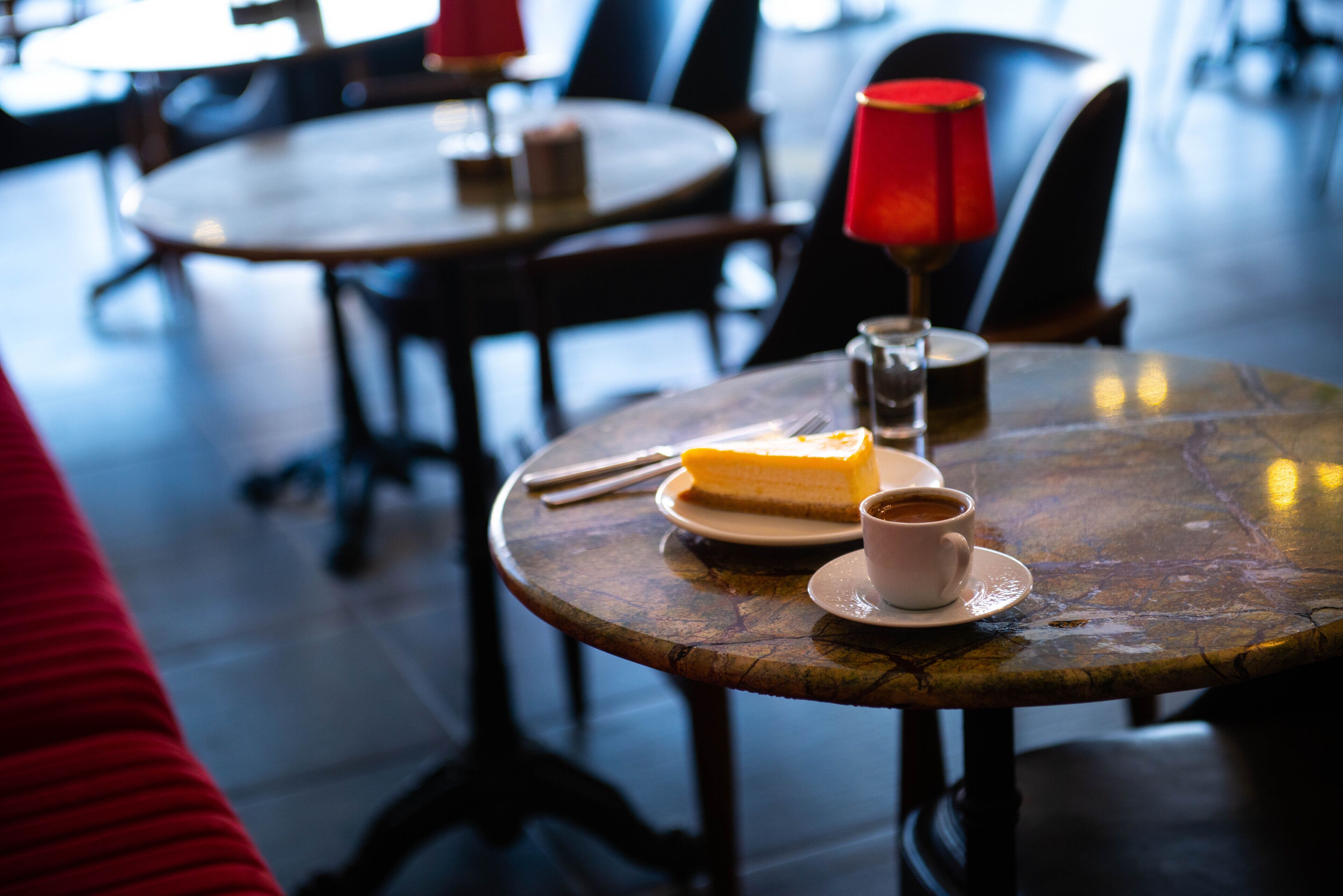 A dining table with a slice of cheesecake, a cup of coffee, and a red candle.
