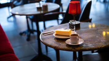A dining table with a slice of cheesecake, a cup of coffee, and a red candle.
