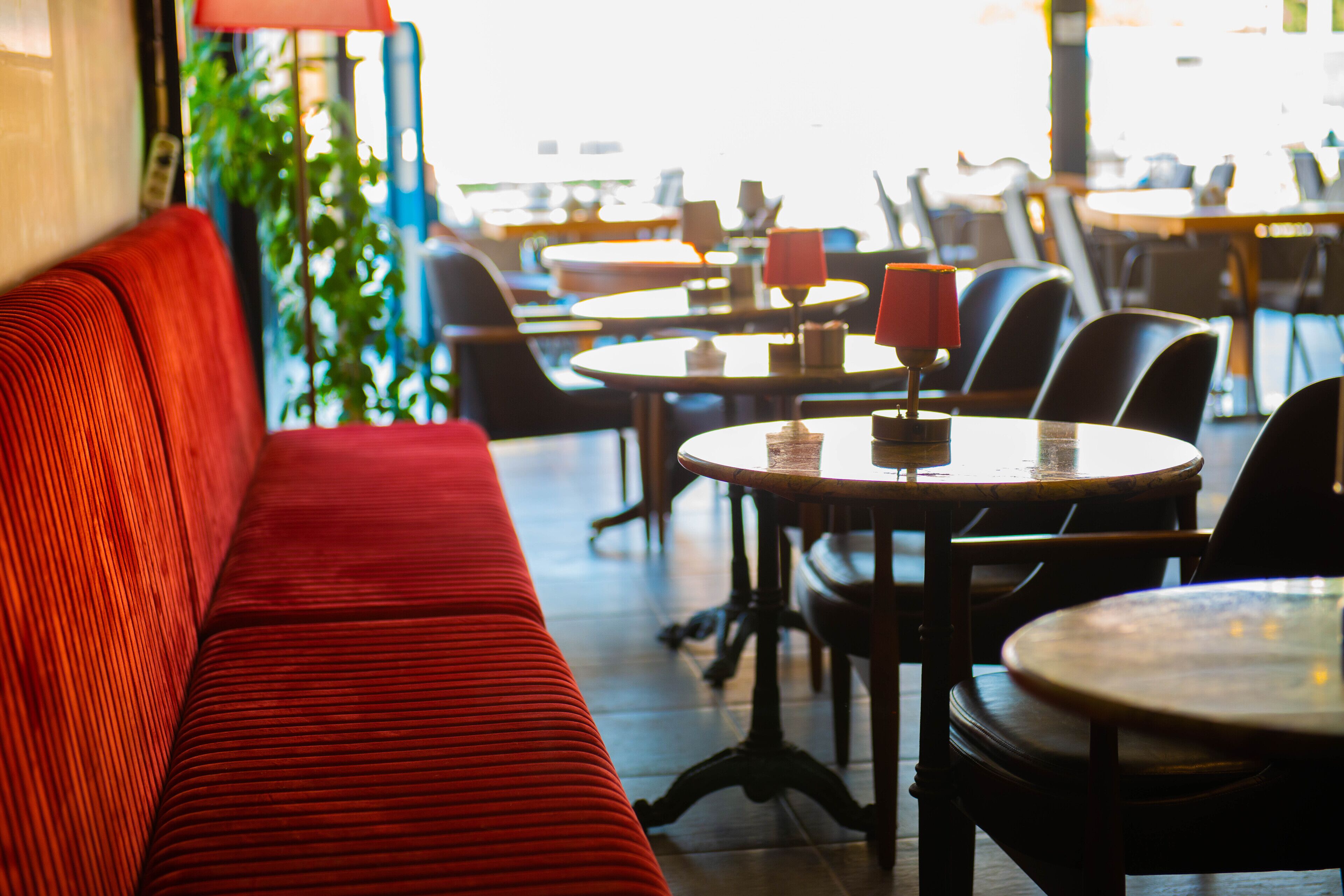 Un interior de restaurante con un banco tapizado de rojo, mesas redondas y sillas.