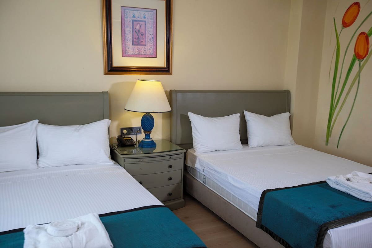 A hotel room with two beds, a nightstand with a lamp, a framed picture on the wall, and a painting of tulips.