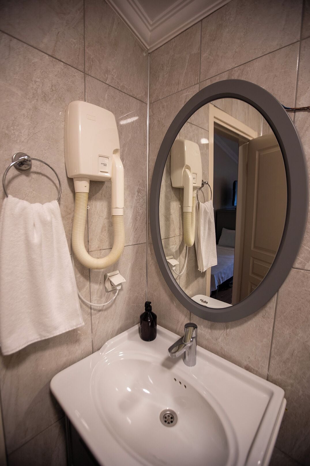 A bathroom with a white sink, a towel ring, a handheld hair dryer, and a mirror.