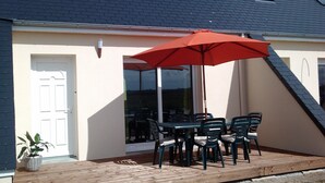 A patio with a table and chairs, a red umbrella, and a potted plant.