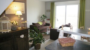 A cozy living room with a sofa, a dining table, and a large window with curtains.