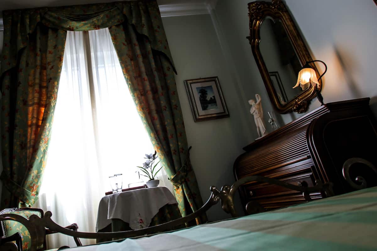 Een kamer met een bed, een dressoir, een spiegel en een raam met gordijnen.