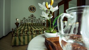 Une pièce avec un lit, un vase blanc rempli de fleurs et une carafe en verre transparent posée sur une table.