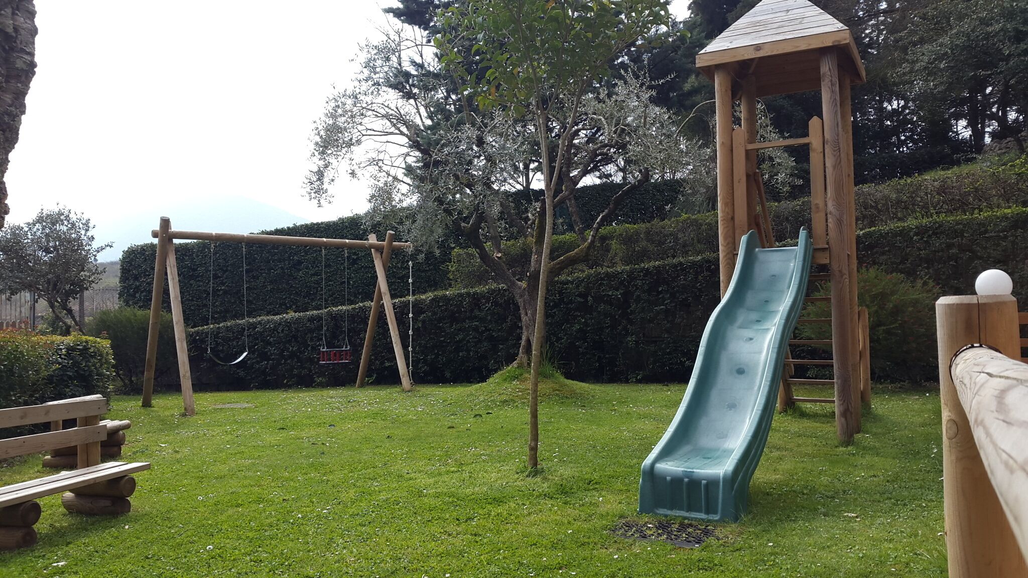 Un'area giochi con uno scivolo, altalene e una struttura in legno.