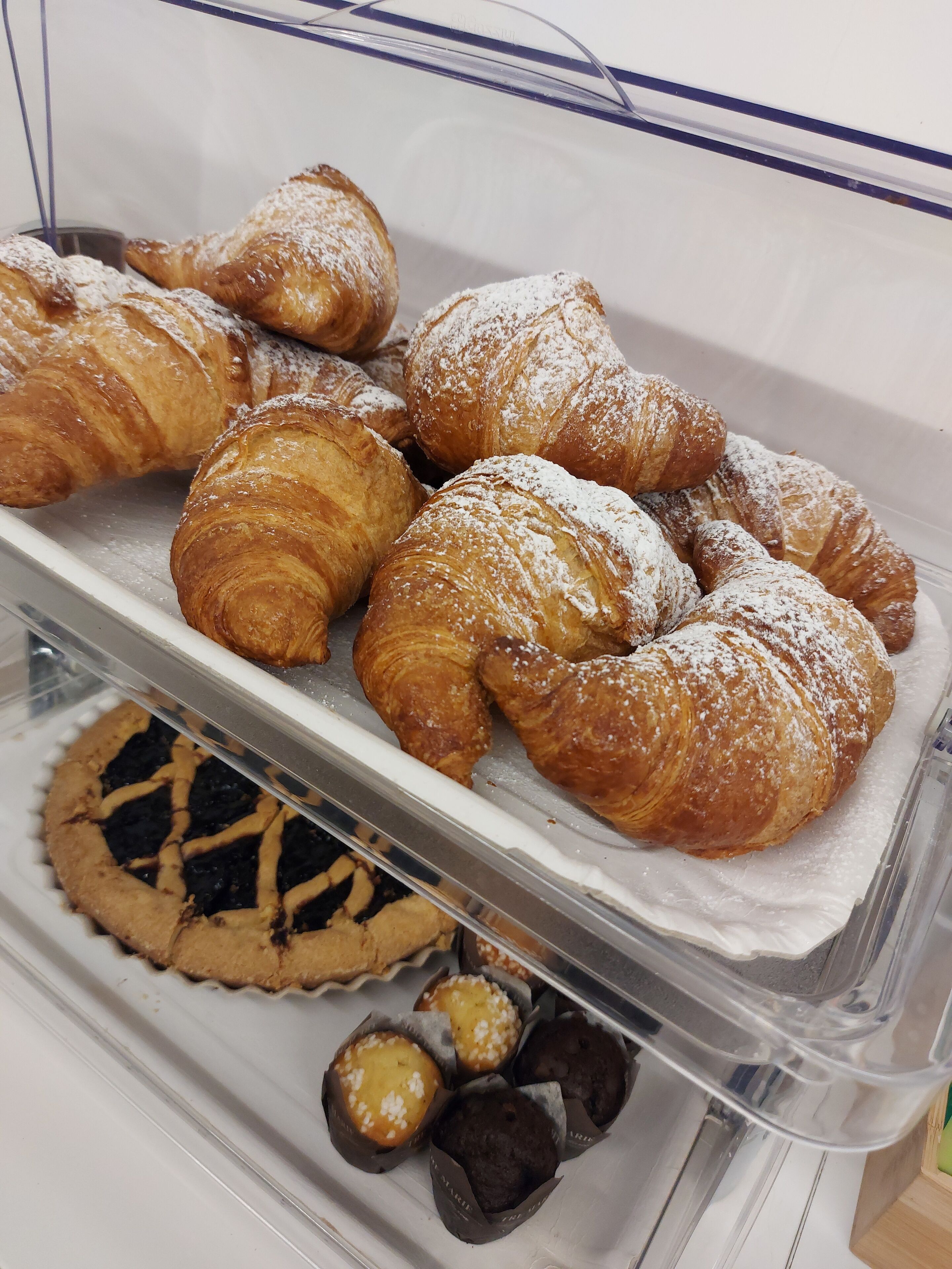Un expositor de panadería con diversos pasteles, incluyendo cruasanes y muffins.