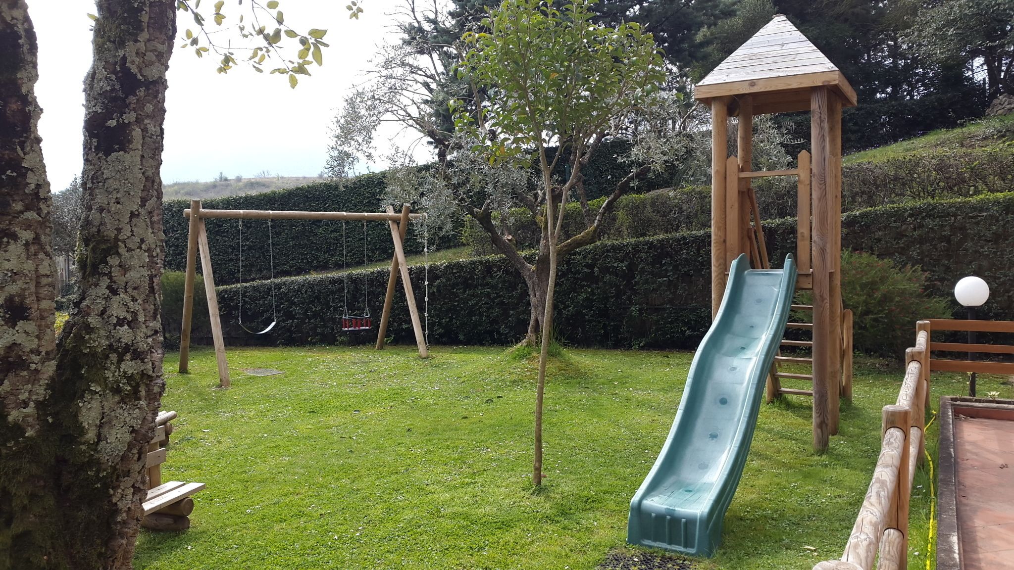 A playground with a slide, swings, and a small wooden structure.