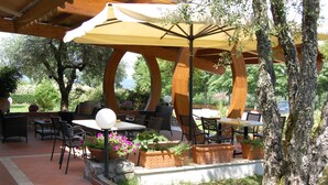 Een terras buiten met houten meubels, een pergola en potplanten.