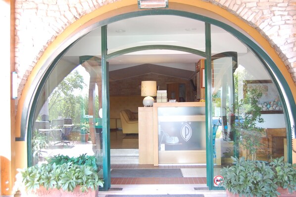 A hotel entrance with a glass door, a reception desk, and potted plants.