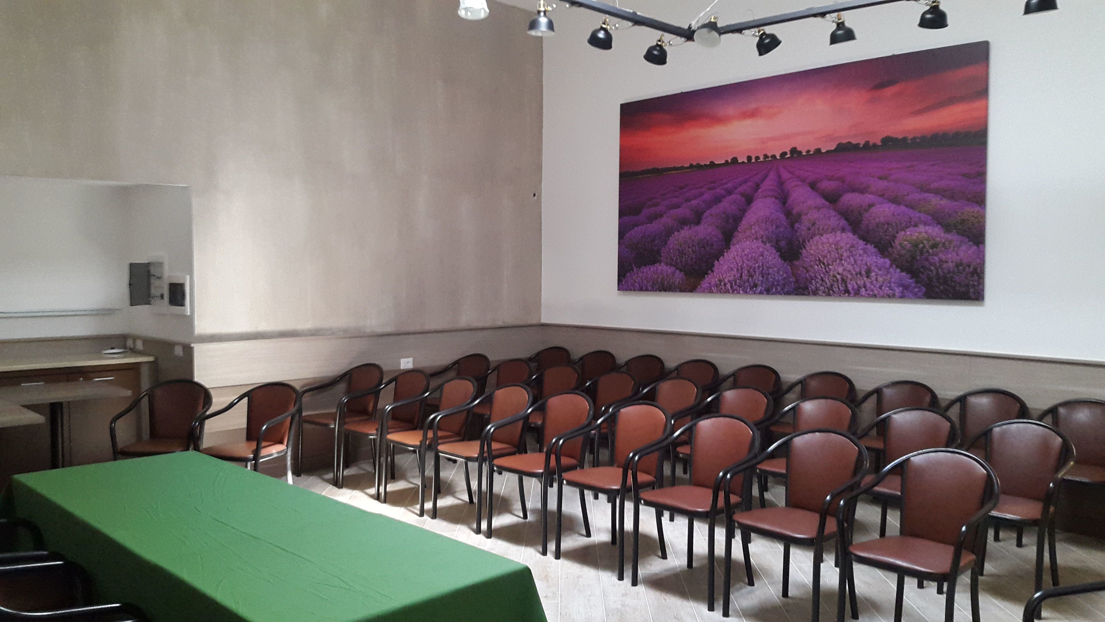 A conference room with rows of chairs, a green table, and a large lavender field painting on the wall.
