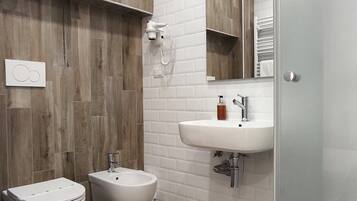 A modern bathroom with a wooden wall panel, white tiles, a sink, a bidet, and a glass shower enclosure.