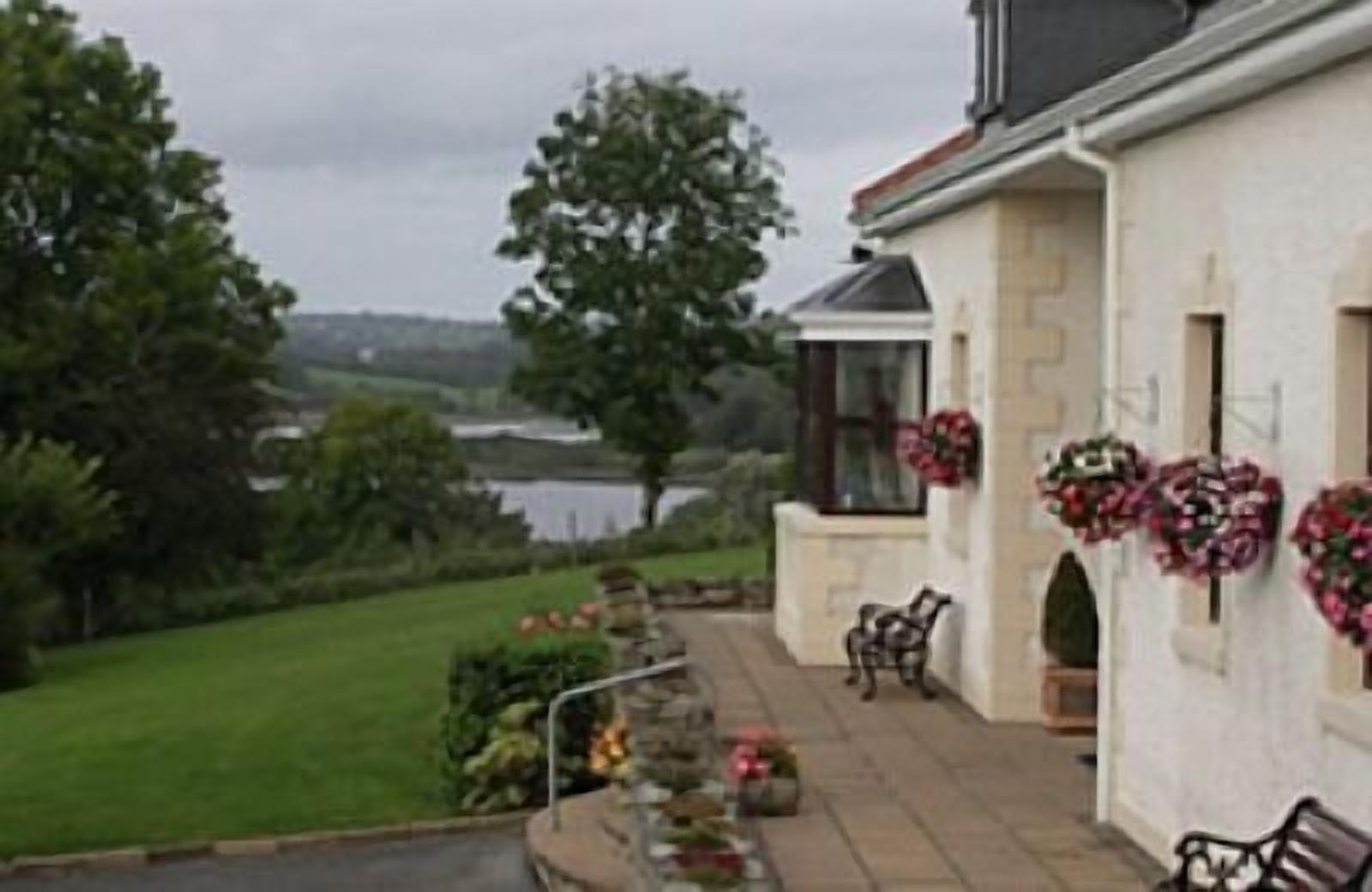A house with a stone facade, a porch with benches, and a view of a lake.