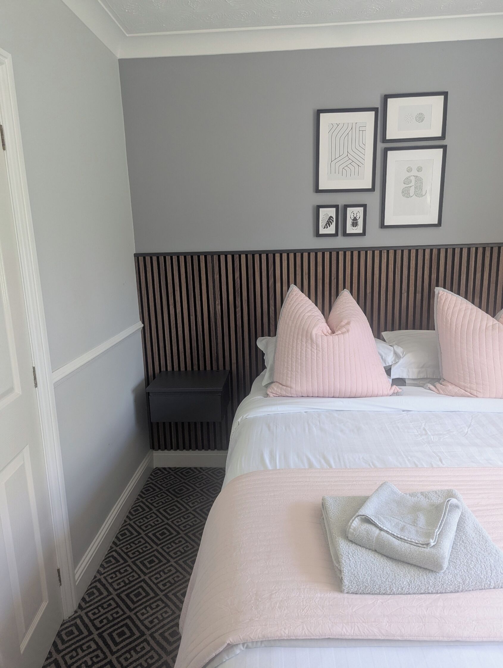 Une chambre d’hôtel avec un lit, une table de chevet, un mur orné de tableaux et un sol à motifs.