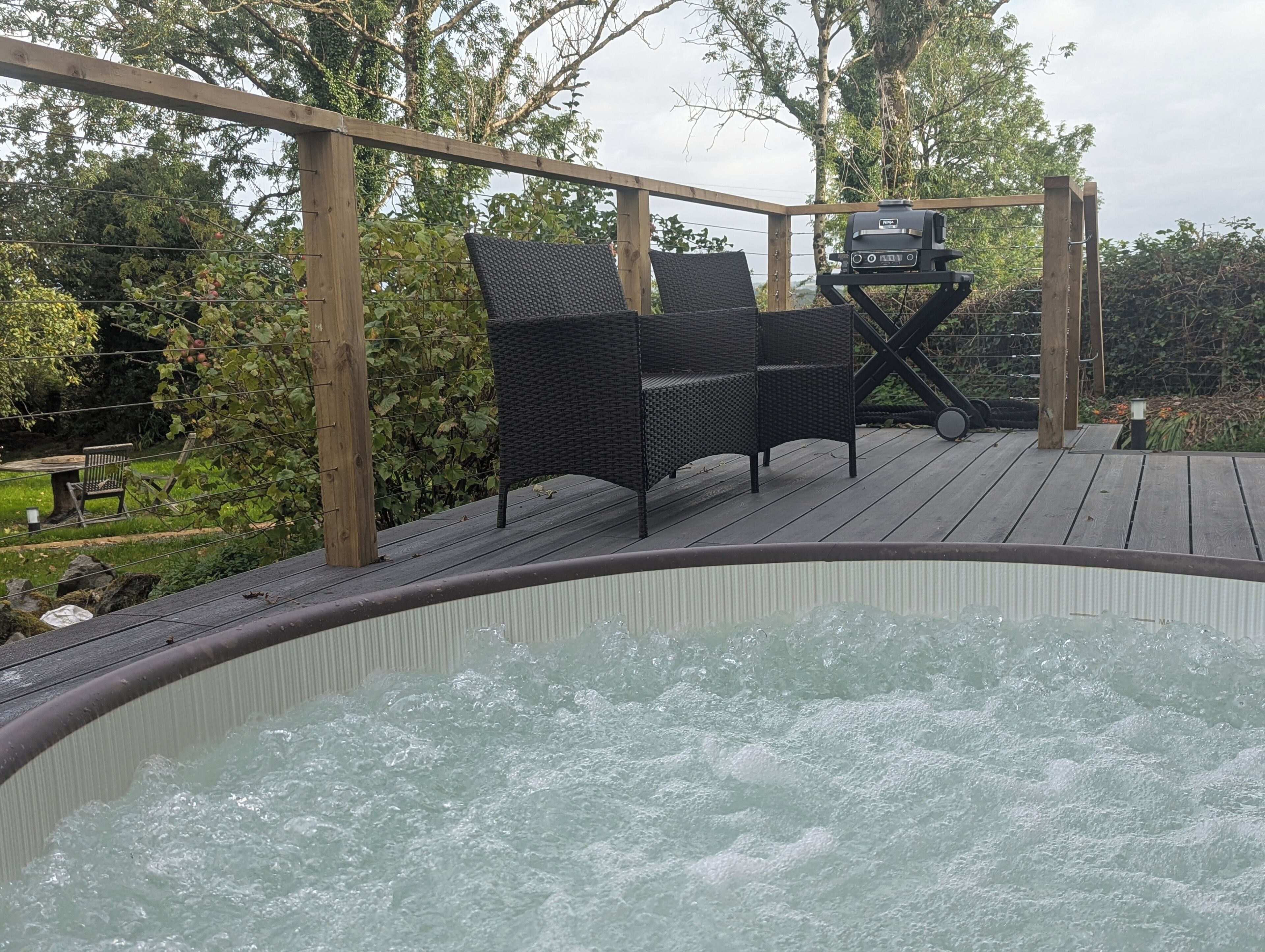 A wooden deck with a hot tub, wicker chairs, and a grill.