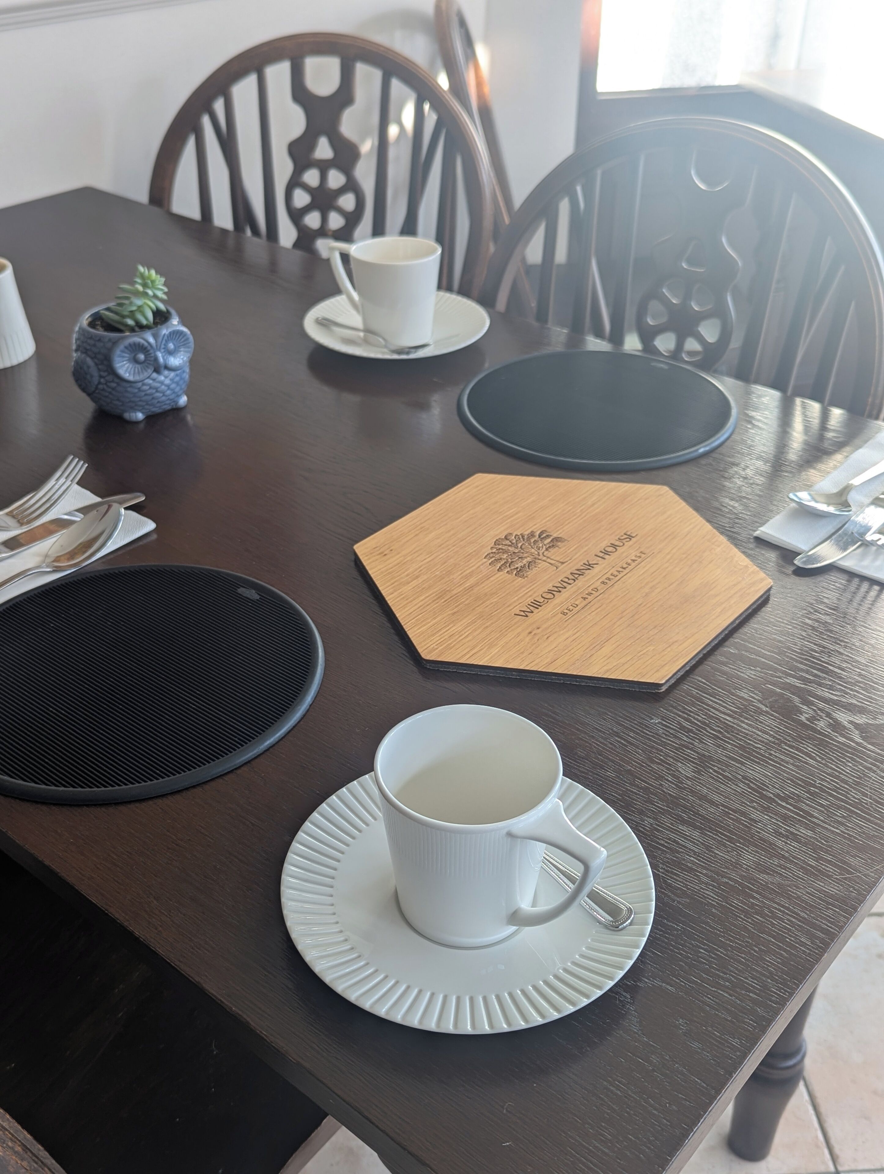 Una mesa de comedor dispuesta con una taza blanca, un plato, cubiertos y un menú.